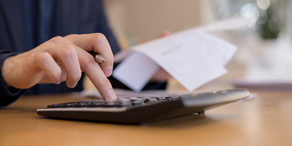A close-up of a person's hands using a calculator and holding paperwork at a desk.